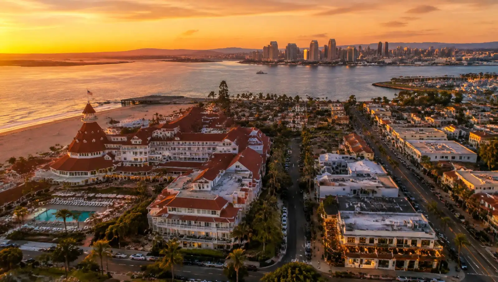 Illustrative image of an aerial view of a seaside resort hotel, a commercial street and a bay skyline at sunset